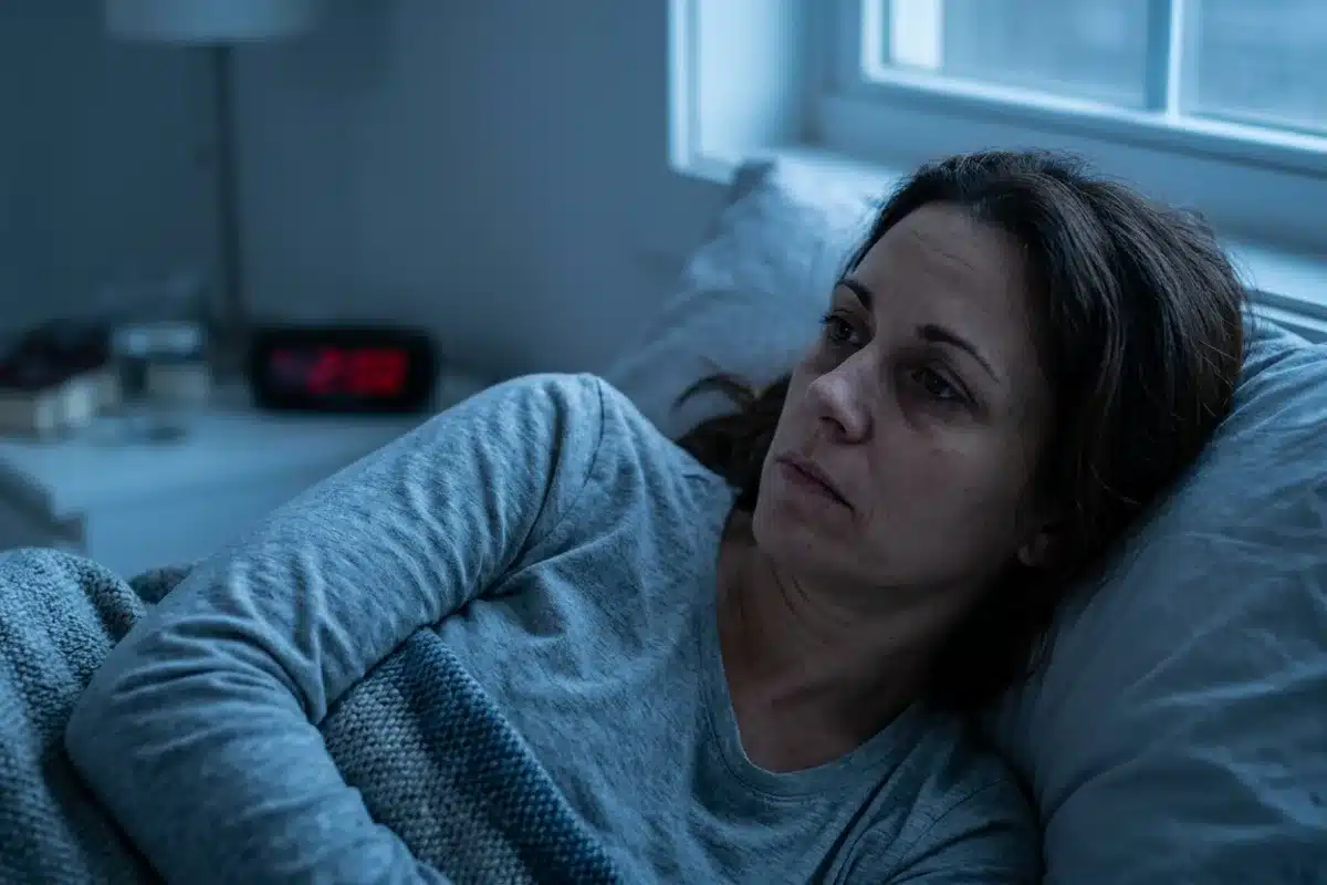Personne éveillée la nuit, insomnie chronique Femme éveillée dans son lit la nuit, illustrant l'insomnie chronique et les réveils nocturnes