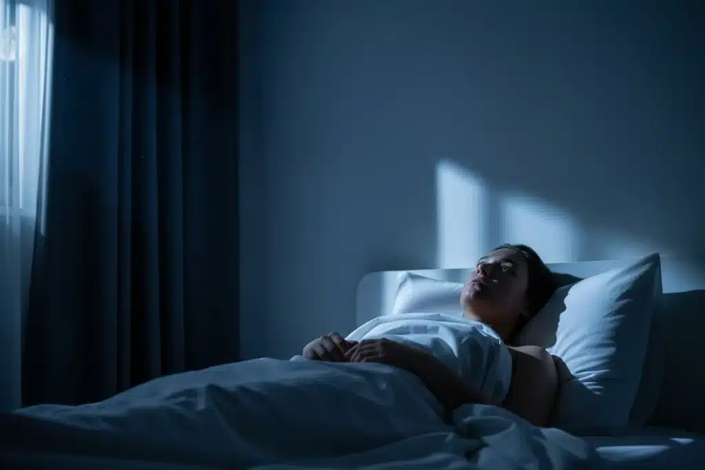 Personne allongée dans son lit les yeux ouverts en pleine nuit, réveillée, chambre éclairée par la lumière de la lune