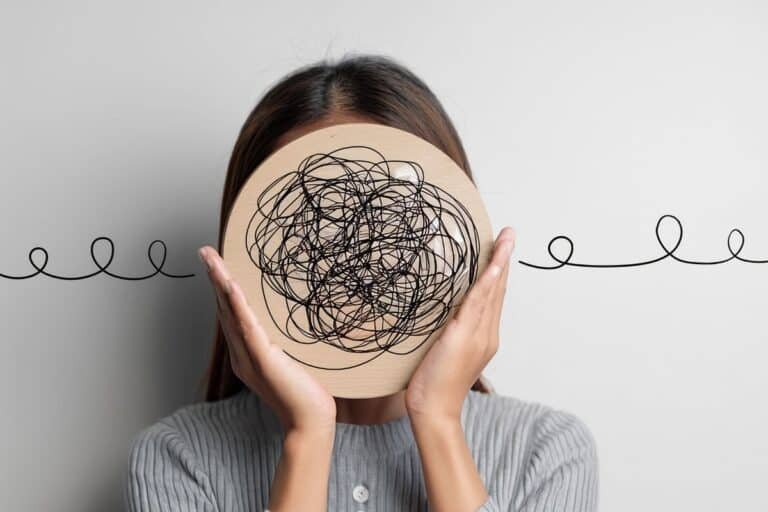 Personne tenant devant son visage un disque couvert de lignes emmêlées, symbole des ruminations mentales et des pensées en boucle